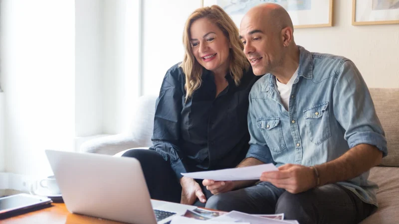 Cheerful couple of clients consulting interior designer through video call. Caucasian man and woman in casual studying wall paint swatches and using laptop. Video call consulting concept